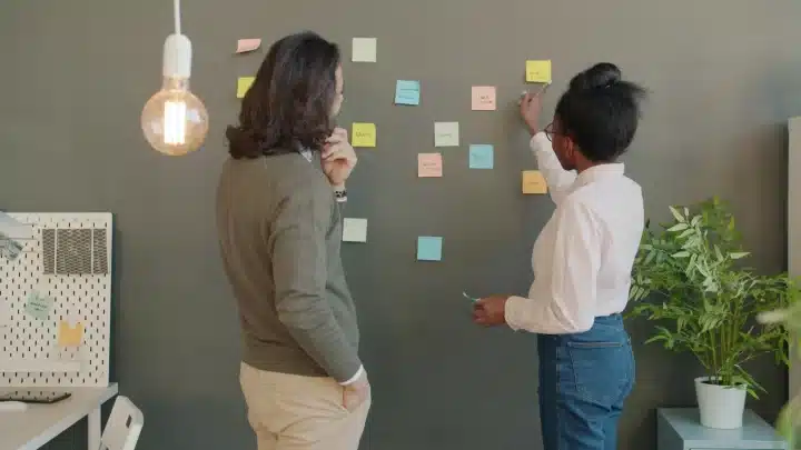 Duas profissionais organizam em post-its as etapas de um plano de 30 dias para reduzir a dependência de indicações