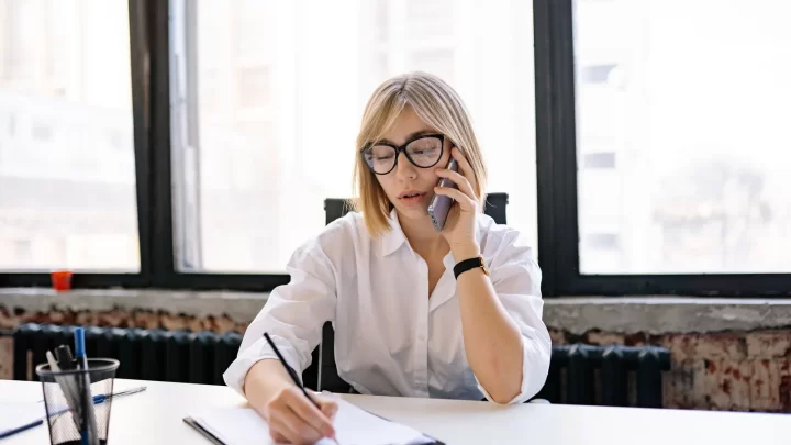 A businesswoman on the phone takes notes at her desk, preparing the next touch with an enterprise decision-maker